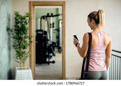 Back View Of Sportswoman Using Smart Phone While Being In A Lobby At Health Club. 