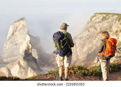 Back view of sporty elderly family hiking on summer. Man and woman in casual clothes and with ammunition looking at mountains. Hobby, active lifestyle concept