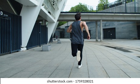 Back View Of Sporty Man Running On Urban Street. Athlete Man Jogging On Training Outdoor. Male Runner Training Run In Slow Motion. Fitness Guy Running At City Street