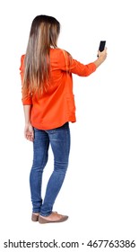 Back View Of Standing Young Beautiful  Woman  Using A Mobile Phone. Girl  Watching. Rear View People Collection.  Backside View Of Person.  Isolated Over White Background. Girl In A Red Jacket Stands