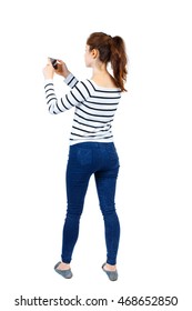 Back View Of Standing Young Beautiful  Woman  Using A Mobile Phone. Girl  Watching. Rear View People Collection.  Backside View Of Person.  Isolated Over White Background. Girl In Striped Sweater