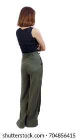 back view of standing young beautiful  woman.  girl  watching. Rear view people collection.  backside view of person. A girl in green trousers stands with her arms crossed