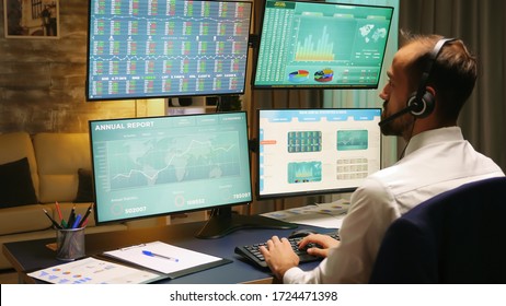 Back View Of Stock Market Trader Looking At Graphs On Multiple Monitors From Home Office.