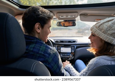 Back view stock photo of happy couple travelling by car on sunny day. View from the backseat. They are looking and smiling at each other. - Powered by Shutterstock