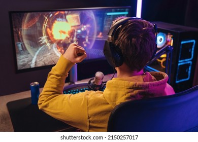 Back view of streamer young man rejoices his victory in esport shooter game tournament, making winner hand gesture. Professional gamer streaming online gameplay competition. Cyber sport concept