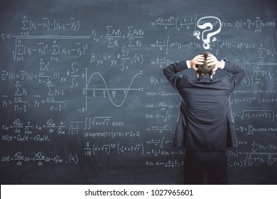 Back view of stressed businessman standing on chalkboard background with mathematical formulas. Science and trouble concept  - Powered by Shutterstock