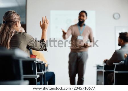 Back view of student raising her hand to answer teacher's question during education training class. 