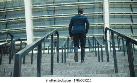 Back view stylish business man going upstairs in suit at street. Successful businessman walking at stairs alone outdoors. Young man walking in luxury suit near stadium. - Shutterstock ID 1786685216