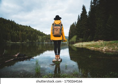 Back view of stylish hipster woman holding flowers,wearing vintage backpack, hat and yellow jacket looking at mountain view while relaxing in nature. Travel and wanderlust concept.Amazing chill moment - Powered by Shutterstock