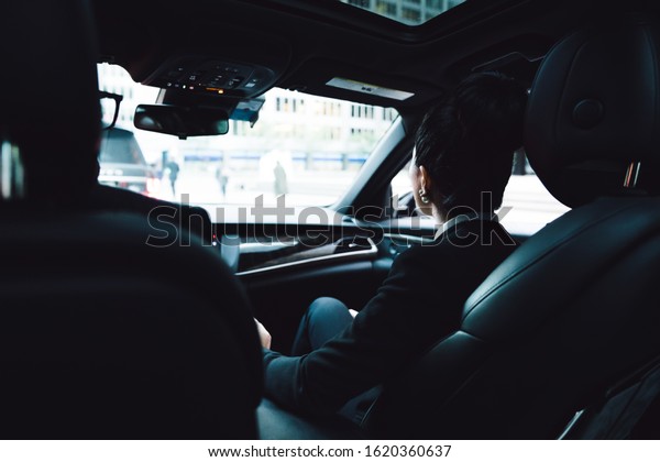 Back\
view of successful coworkers in formal wear focusing on road while\
riding to work during traffic jam in company\
car