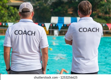 Back view of swimming coaches, wearing COACH shirt, working together at an outdoor swimming pool - Powered by Shutterstock