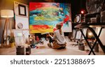 Back view of talented concentrated Caucasian woman professional artist sitting on floor in studio in evening painting drawing on big canvas, creativity work, contemporary creative painter