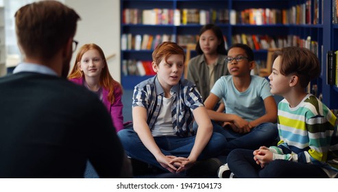 Back view of teacher with class visiting library discussing books for education. Multiethnic schoolchildren having lesson with teacher in modern library - Powered by Shutterstock