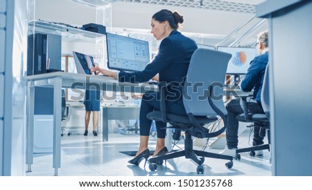 Back View of Team of Technology Engineers Working on Desktop Computers in Bright Office. Screens Show IDE / CAD Software, Implementation of Machine Learning, Neural Networking and Cloud Computing