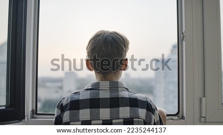 Back view of teen boy looking through window, sad orphan kid waiting on adoption