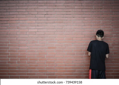 back view of teenage Asian boy standing in front of red brick wall background, copy space, teenager problem concept - Shutterstock ID 739439158