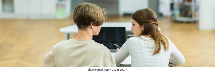 Back View Of Teenage Friends Talking Near Laptop With Blank Screen In Library, Banner