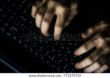 Back View of Teenage Hacker Working in Computer and Infecting with Virus Data Servers of Government Infrastructures. His Hideout is Dark with Many Monitors Around.