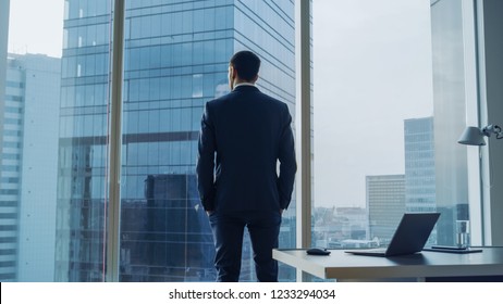 Back View of the Thoughtful Businessman wearing a Suit Standing in His Office, Hands in Pockets and Contemplating Next Big Business Deal, Looking out of the Window. Big City Business District View - Shutterstock ID 1233294034