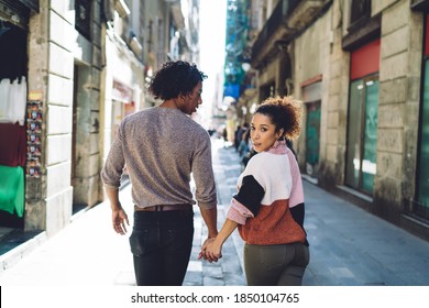 Back view of thoughtful young African American man and ethnic woman in casual clothes holding hands while strolling along city street on sunny day - Powered by Shutterstock