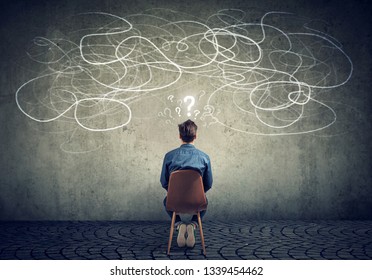 Back view of a thoughtful young businessman sitting on chair looking at a scribble on a wall feeling confused with too many questions  - Powered by Shutterstock