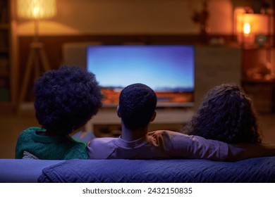 Back view of three people sitting on couch together and watching TV in dark room - Powered by Shutterstock