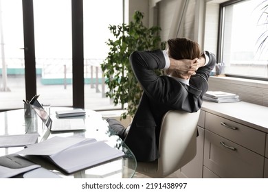Back view of tired businessman sit lean in chair in office relax relieve negative emotions after working day. Exhausted calm male employee rest at workplace, daydream or nap. Stress free concept.