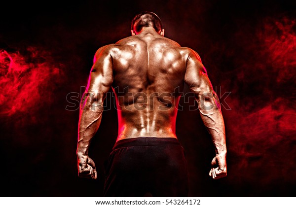 The back view of torso of attractive male\
body builder on dark smoky\
background.
