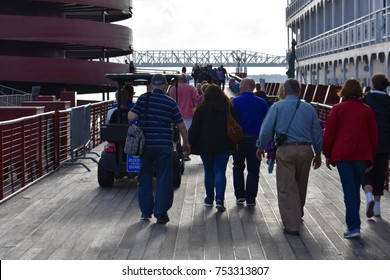 Back view of tourists walking down boardwalk with bridge in distance and cruise ship on side