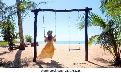 Back view of travel woman in hat sitting on swing on the beach with palm trees and turquoise sea on background. Summer vacation, tropical holidays - Shutterstock ID 2179762215