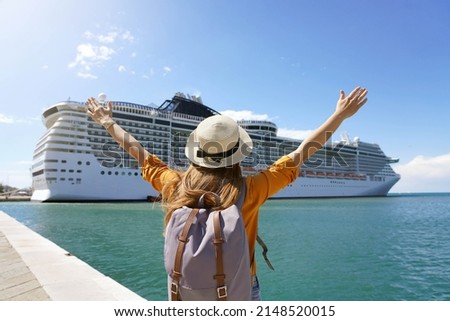Back view of traveler girl with raised arms standing in front of big cruise liner