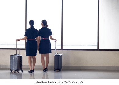 Back view two Cabin crew or air hostess in airport. Cabin crew, air hostess working in airplane. Service mind. Asian stewardess with suitcase at modern airport terminal. flight attendant