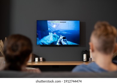 Back view of two contemporary siblings sitting in front of tv set and playing video game in living-room during vacations or on weekend