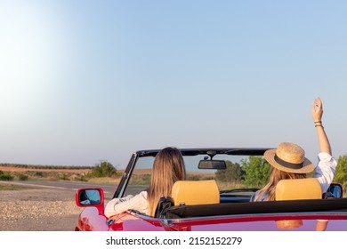 Back View Of Two Friends Having Fun Driving A Vintage Red Car In The Countryside During Spring Break With Copy Space