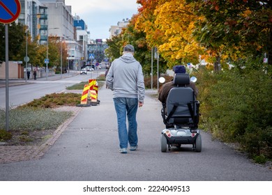Back view of two men. Other is walking and other one is moving with electric wheelchair.