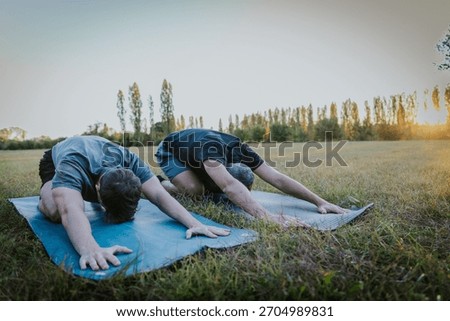 Back view of two men in child’s pose stretching on yoga mats outside.