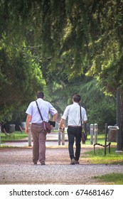 back view of two men walking at park, they wearing an elegant white shirt and working bag