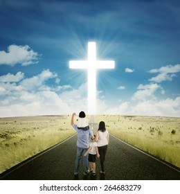 Back view of two parents standing on the road with their children looking at a cross