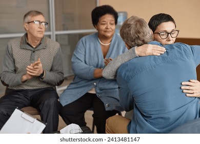 Back view of two senior people embracing in group therapy session supporting each other with mental health struggles, copy space - Powered by Shutterstock