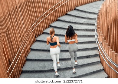 Back view of two sporty women friends in tops and leggings running on stairs on the street. Outdoor training. The concept of sports, jogging and a healthy lifestyle. - Powered by Shutterstock