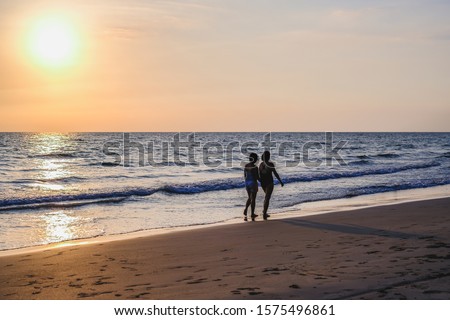 The back view of two women wearing bikinis walking on the beach vacations travel holiday, Beautiful sunset background.