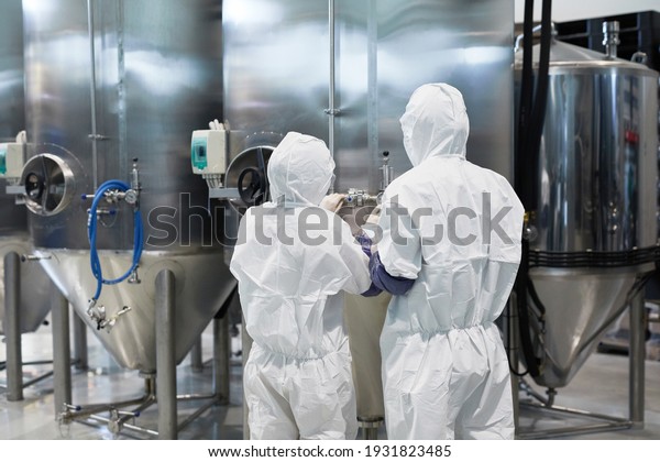Back view at two\
workers wearing protective suits while using machines at modern\
chemical plant, copy space