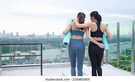 Back View Two Young Asian Women In Gym Clothes Walking Holding Yoga Mats Preparing To Exercise Outdoors