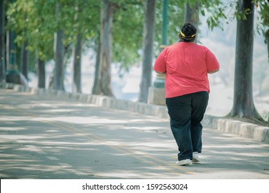 Back view of unidentified fat man wearing sportswear while jogging in the middle of the roads