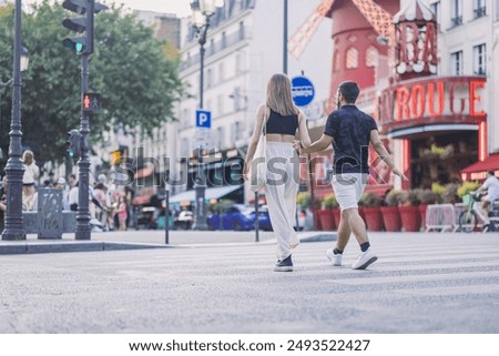 Back view of an unknown couple crossing the road in front of famous moulin rouge landmark in paris. Couples sightseeing