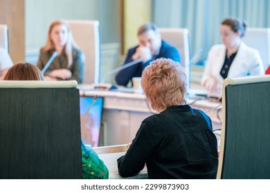 Back view of unrecognizable businesswoman sitting at round table near colleagues with microphones during conference in spacious hall