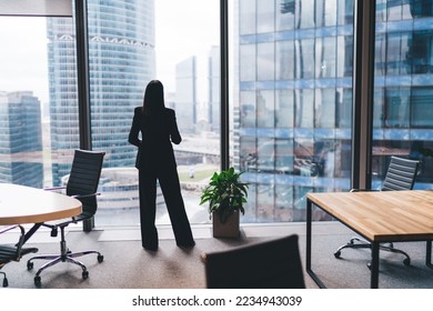 Back view of unrecognizable female entrepreneur in formal clothes standing near glass wall and office furniture at workplace while looking away at cityscape - Powered by Shutterstock