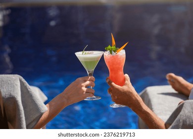 Back view of unrecognizable male and female toasting with cocktails while celebrating vacation and sitting at poolside of resort hotel - Powered by Shutterstock