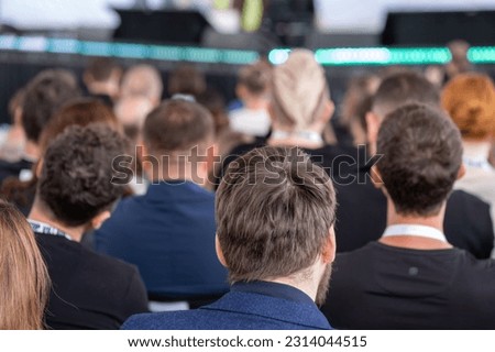 Back view of unrecognizable people in smart casual clothes sitting in conference hall and listening to speaker