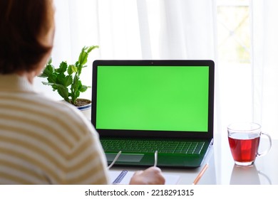 Back View Of Unrecognizable Senior Elderly Woman At The Table Holding Glasses And Watching Educational Webinar, Online Lecture Seminar On Laptop With Green Screen. The Concept Of Distance Education